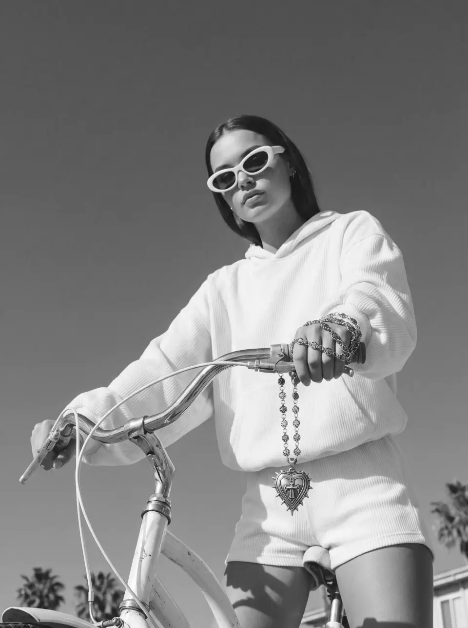 Woman in white sunglasses and a cream hoodie riding a bicycle