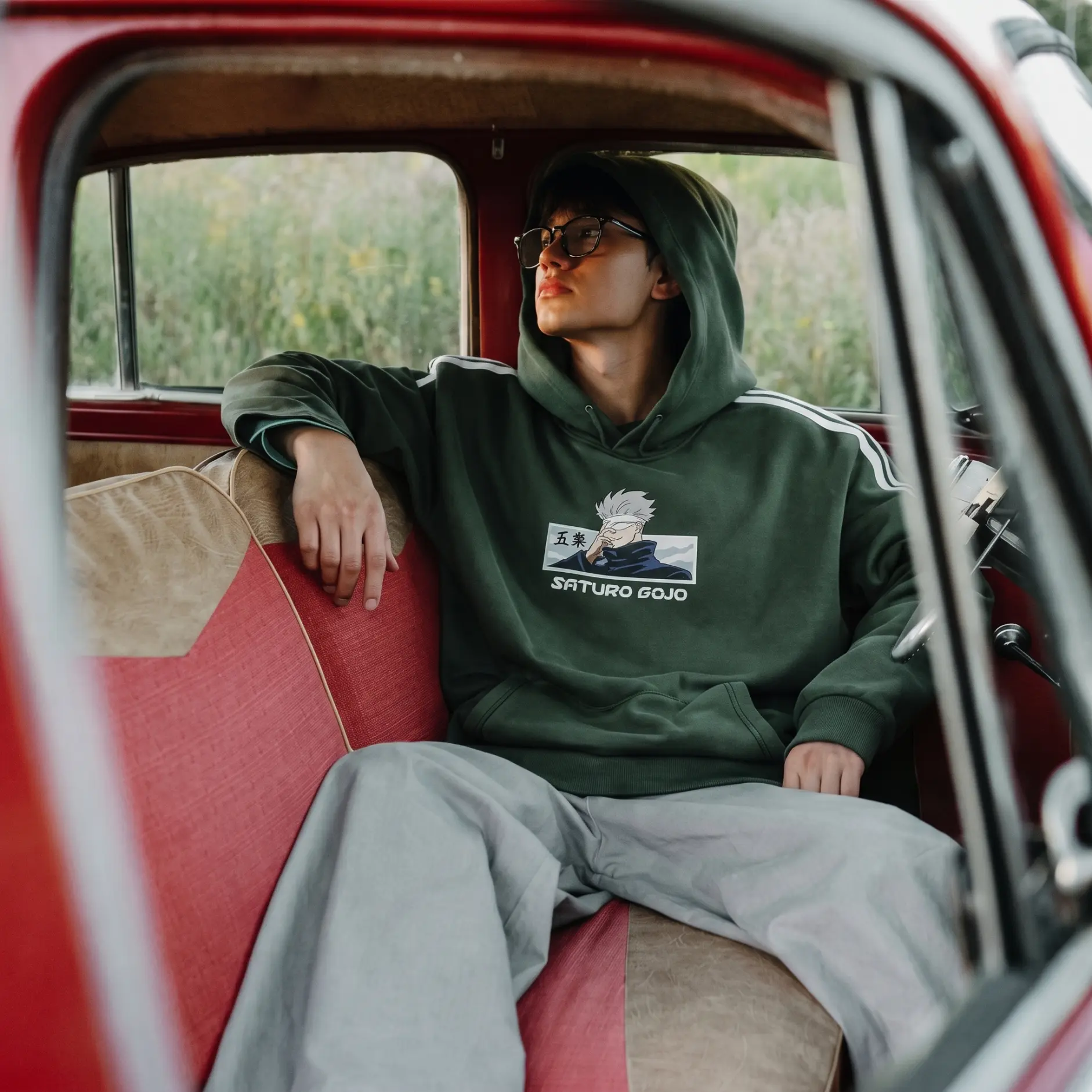 Model in a green hoodie sitting inside a vintage red car