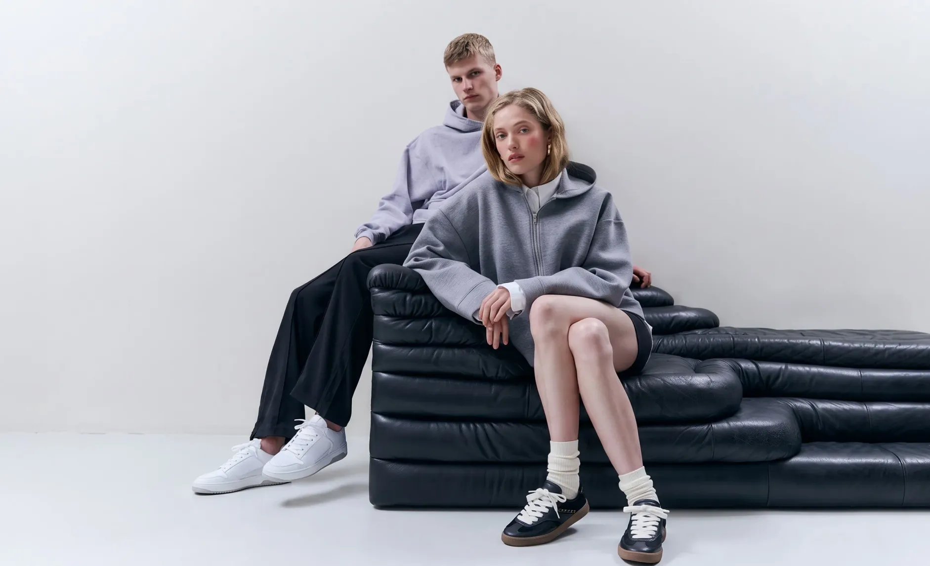 Two models in grey hoodies on a black leather sofa